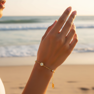Hand wearing a gold bracelet with a sunset or sunrise over water in the background