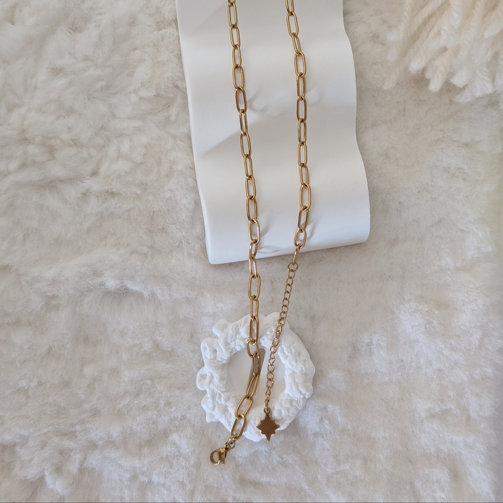 Gold chain necklace on a white ribbon against a beige background