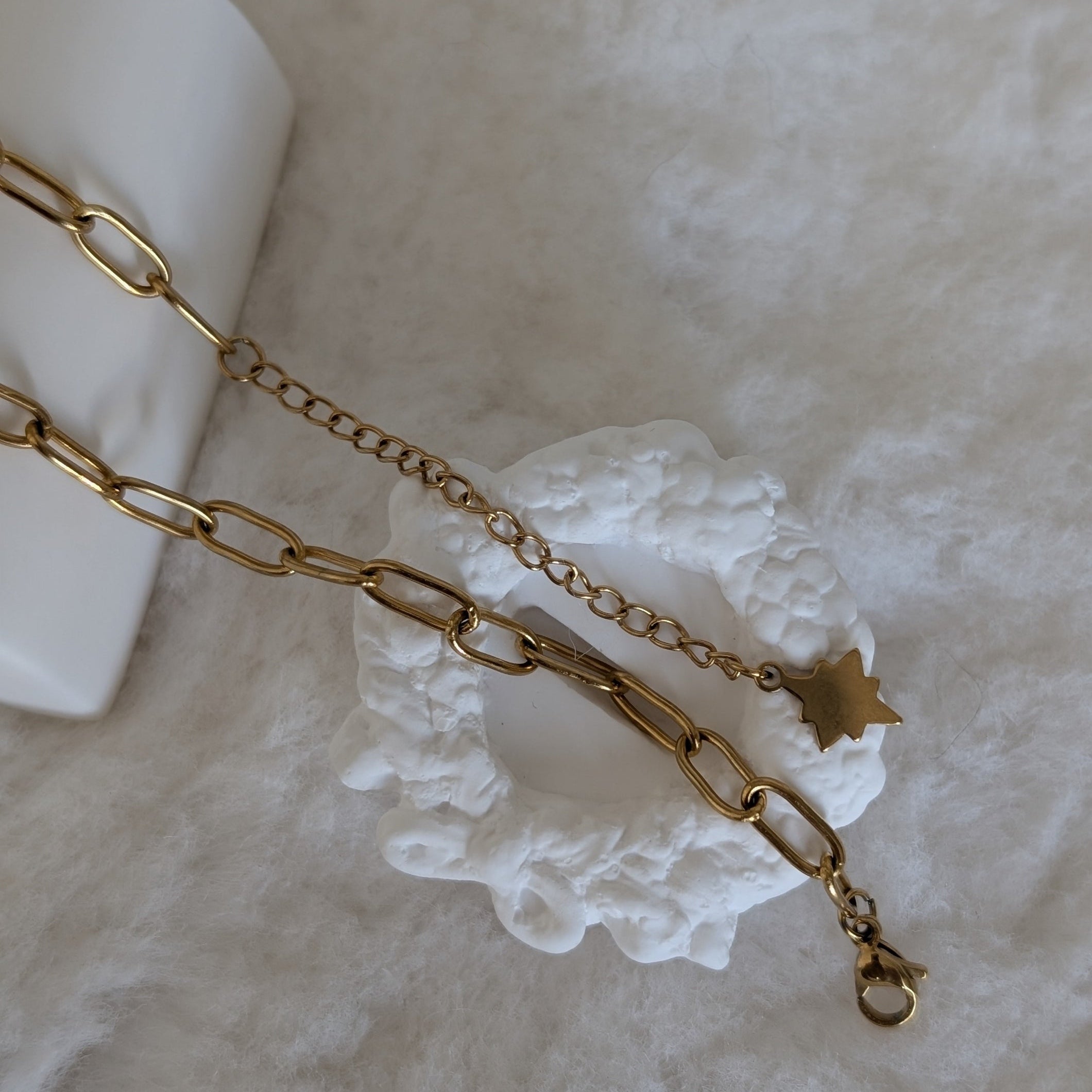 Gold chain bracelet with a star charm on a white ceramic dish