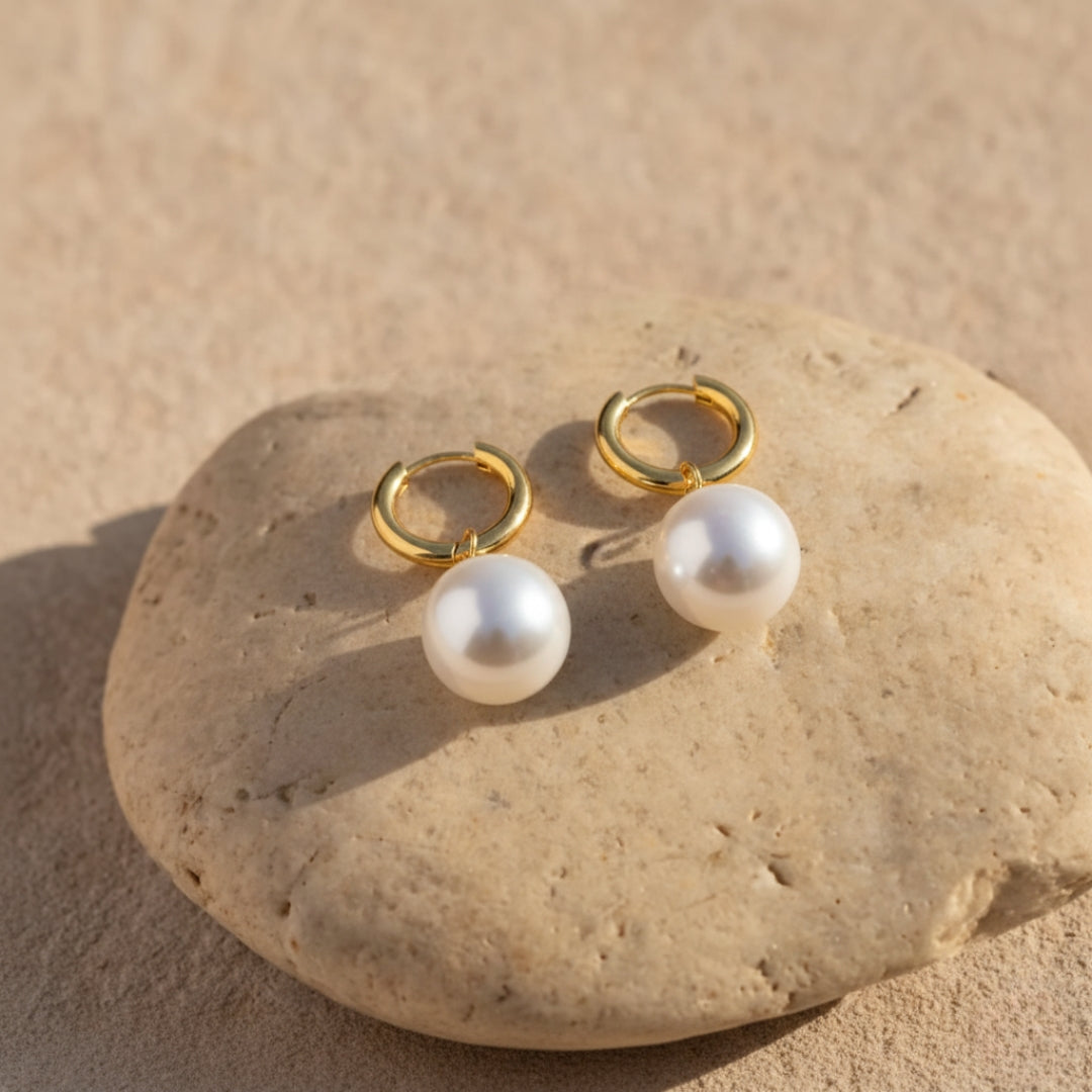 Pearl earrings with gold loops on a stone surface
