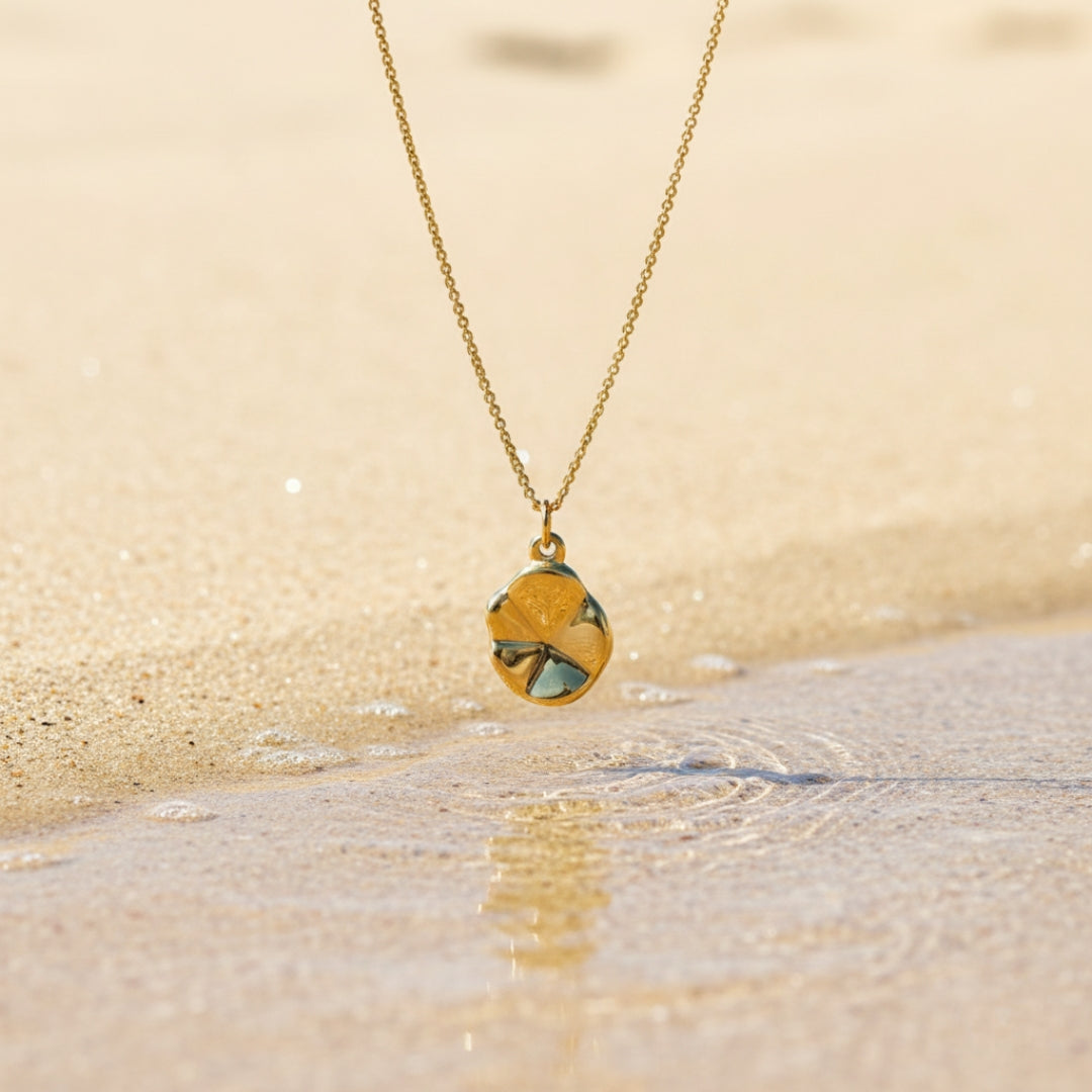 Gold necklace with a pendant on a sandy beach