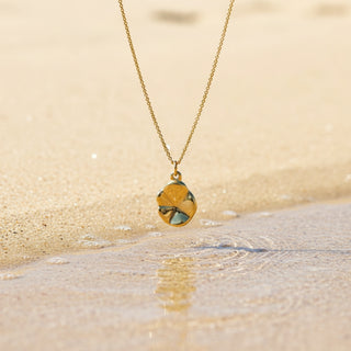 Gold necklace with a pendant on a sandy beach