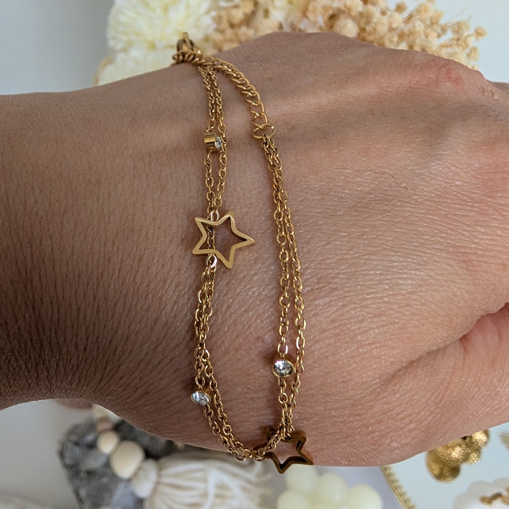 Gold bracelet with star charm on a wrist against a neutral background