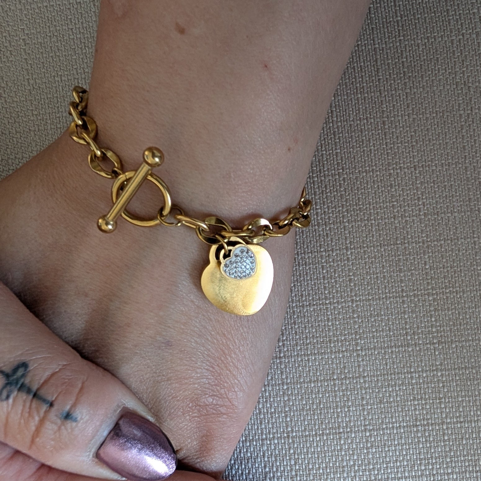 Gold bracelet with charms on a wrist against a neutral background