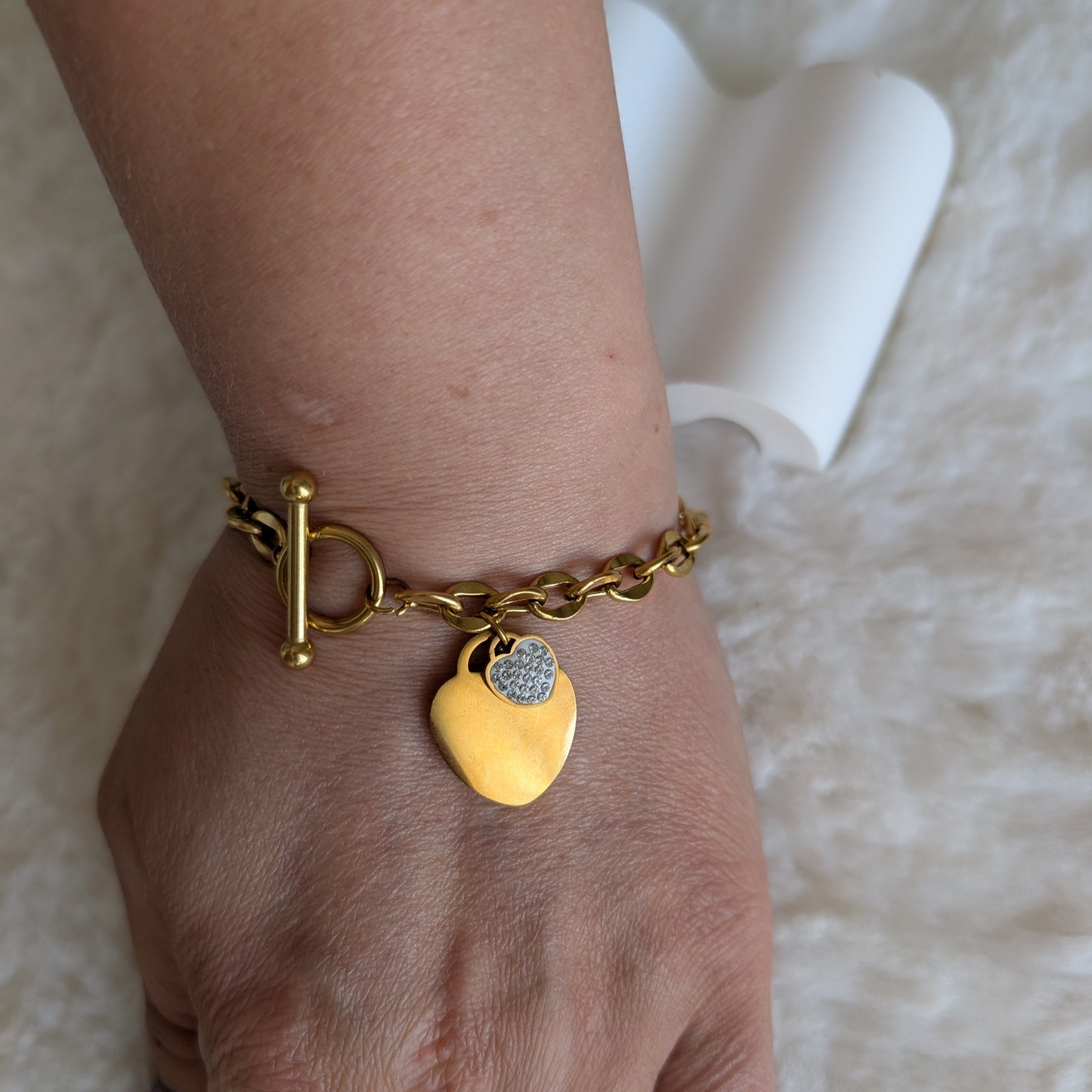 Gold bracelet with a heart-shaped charm on a wrist against a soft background