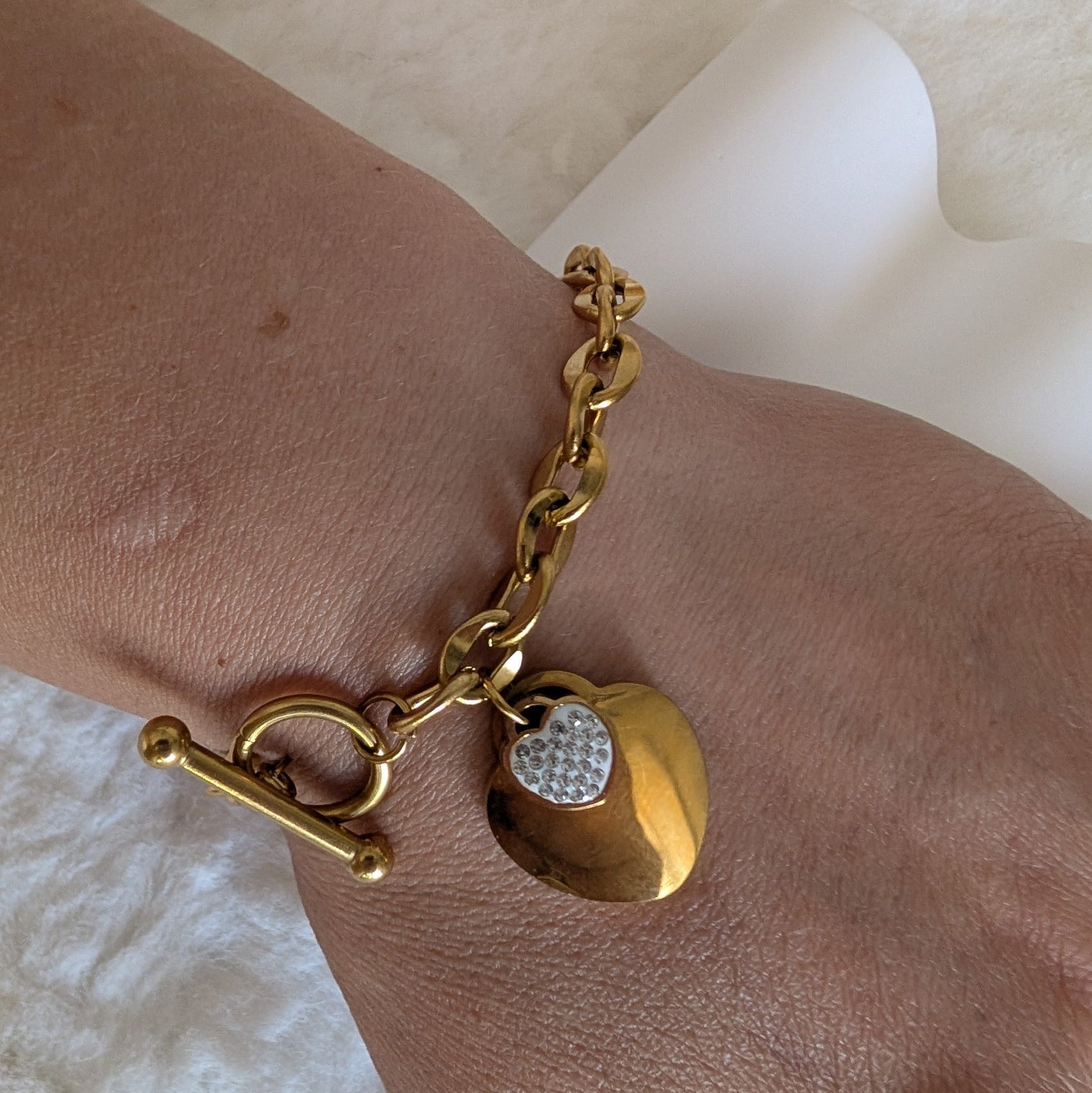 Gold bracelet with heart-shaped charm on a wrist against a white background
