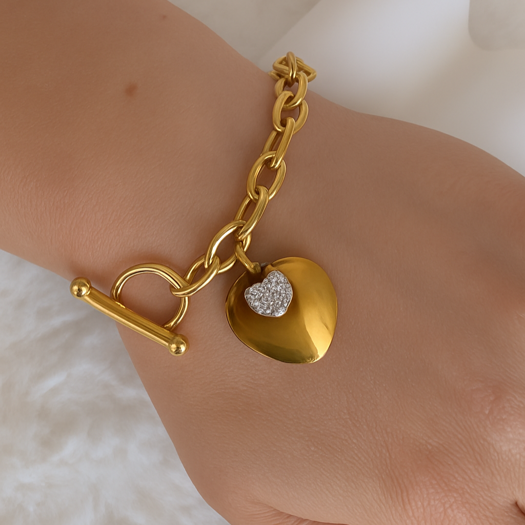 Gold bracelet with heart-shaped charm on a wrist against a soft background