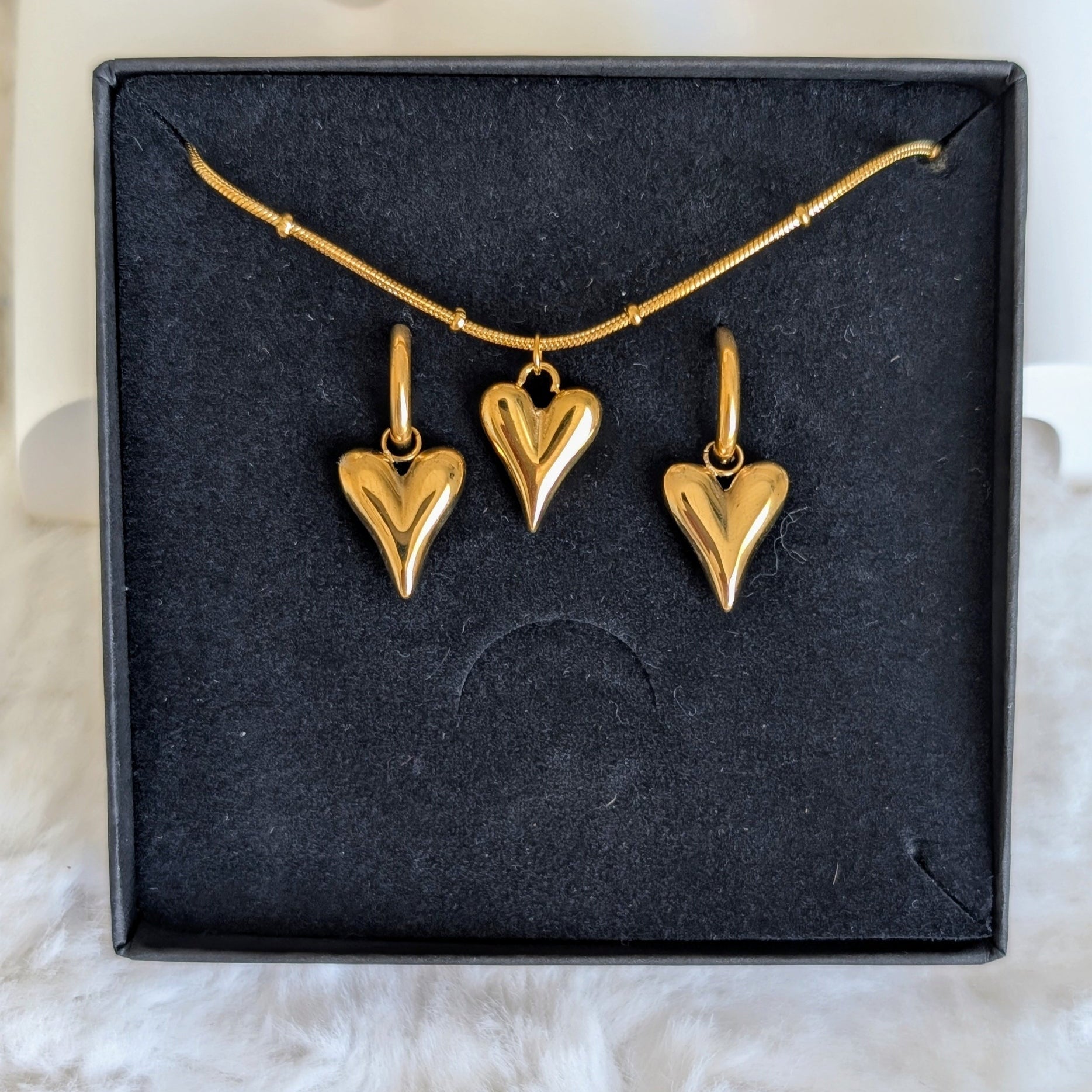 Gold necklace with heart pendants on a black display card.