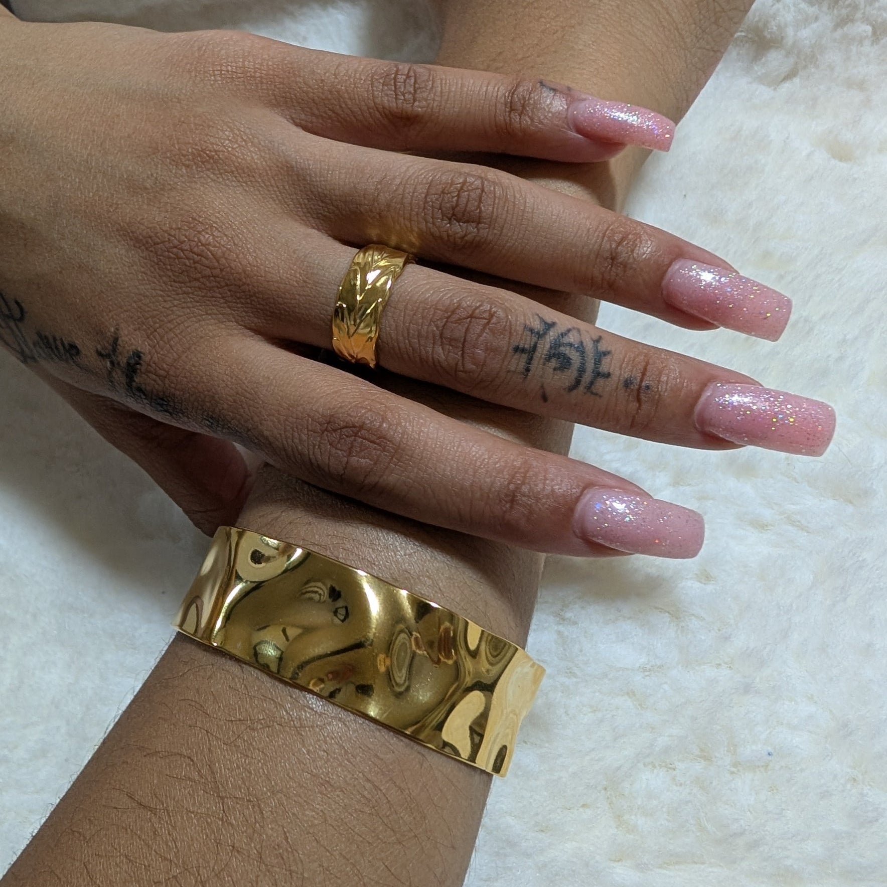 Hand wearing a gold ring and bracelet on a textured white background