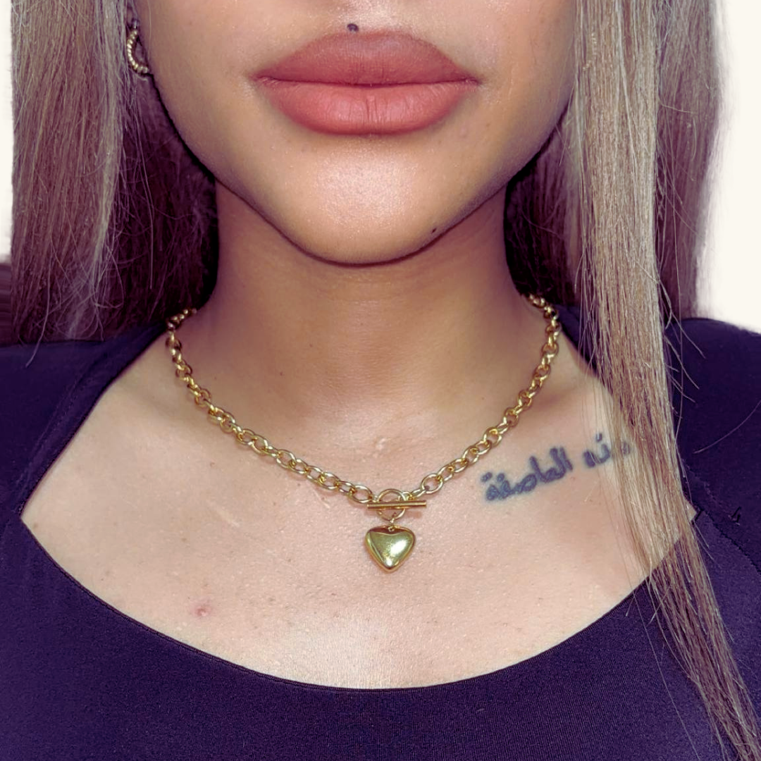 Close-up of a person wearing a gold chain necklace with a heart pendant.
