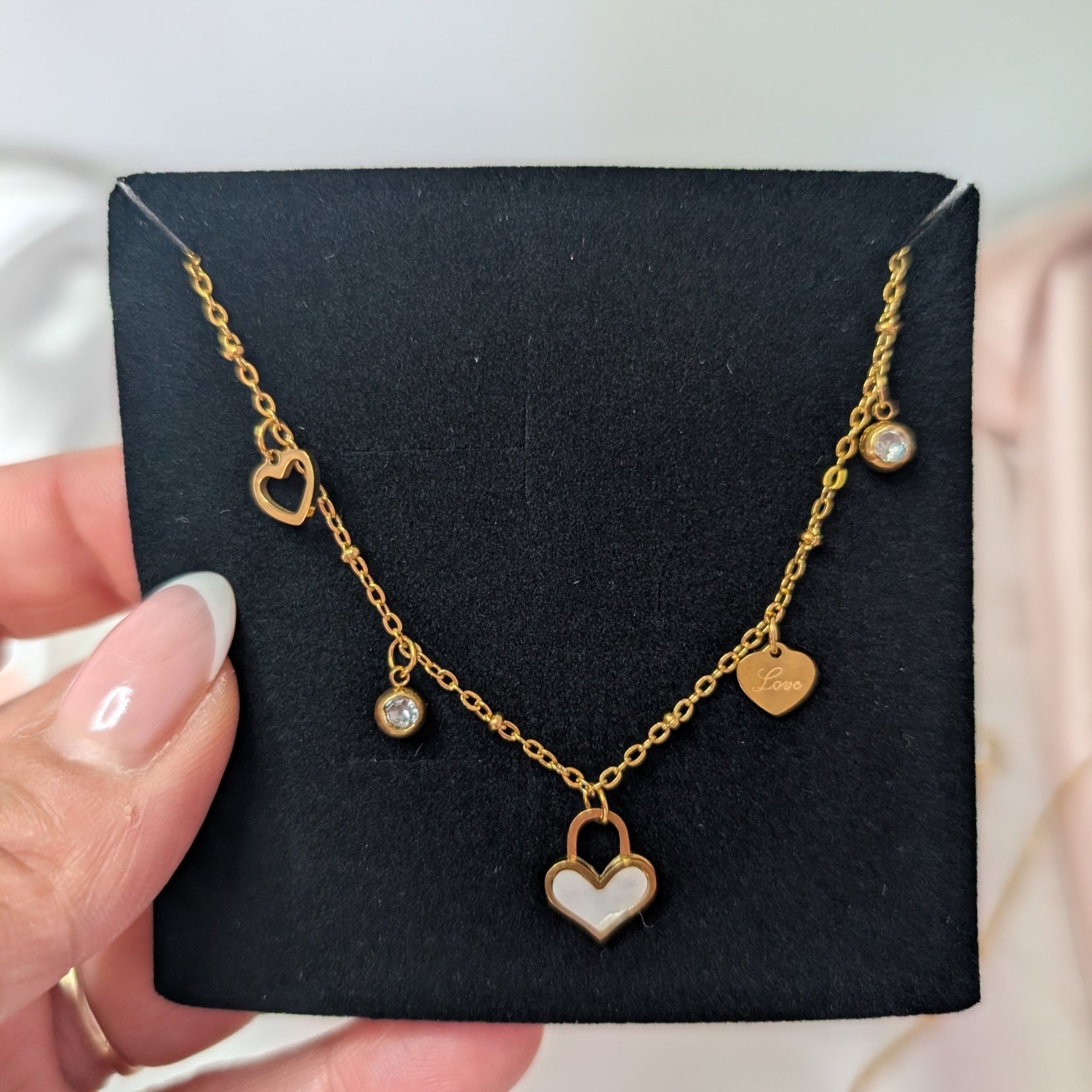 Gold necklace with heart pendant on a black card held by a hand.