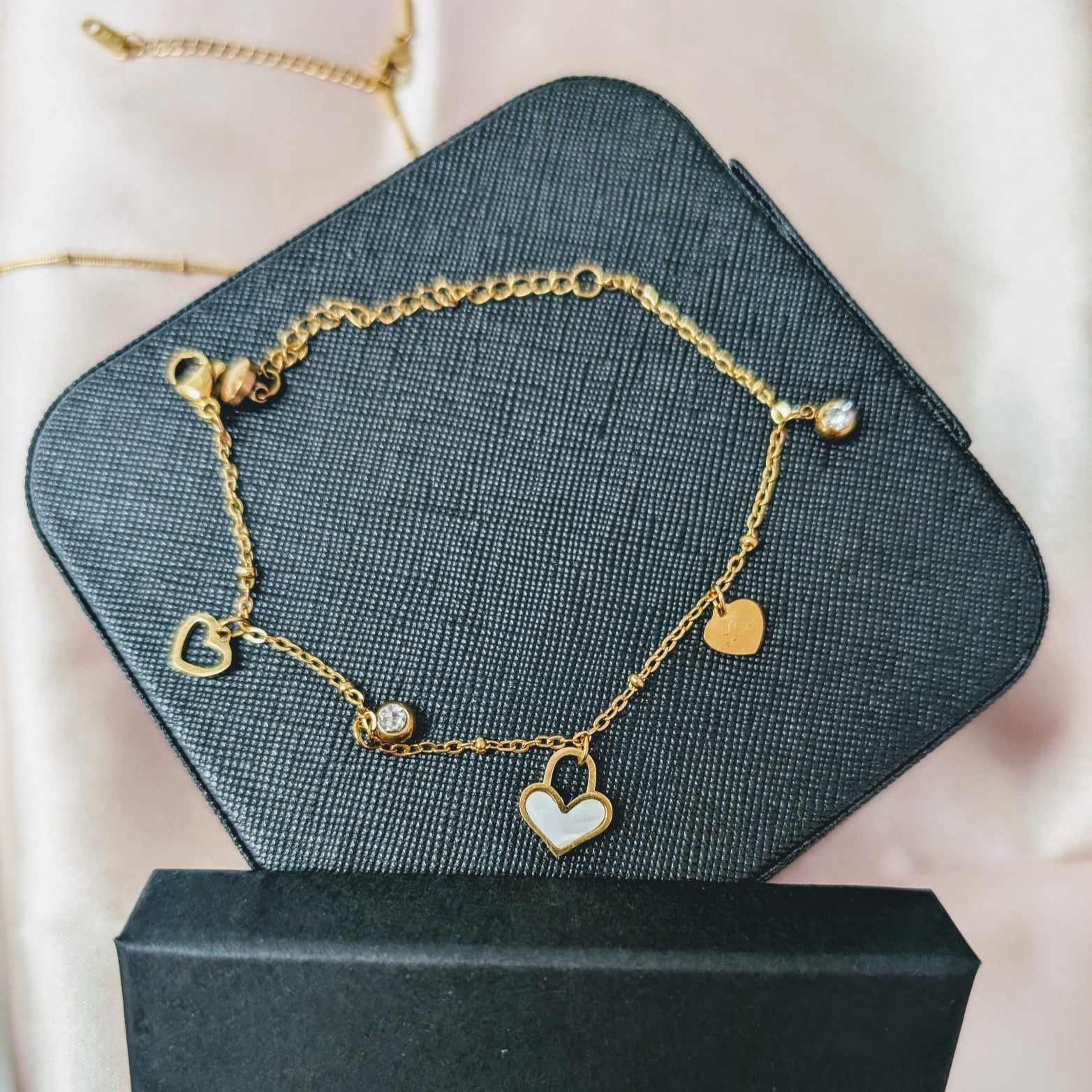 Gold bracelet with heart and pearl charms on a black jewelry box with 'Carolein Jewelry' branding.