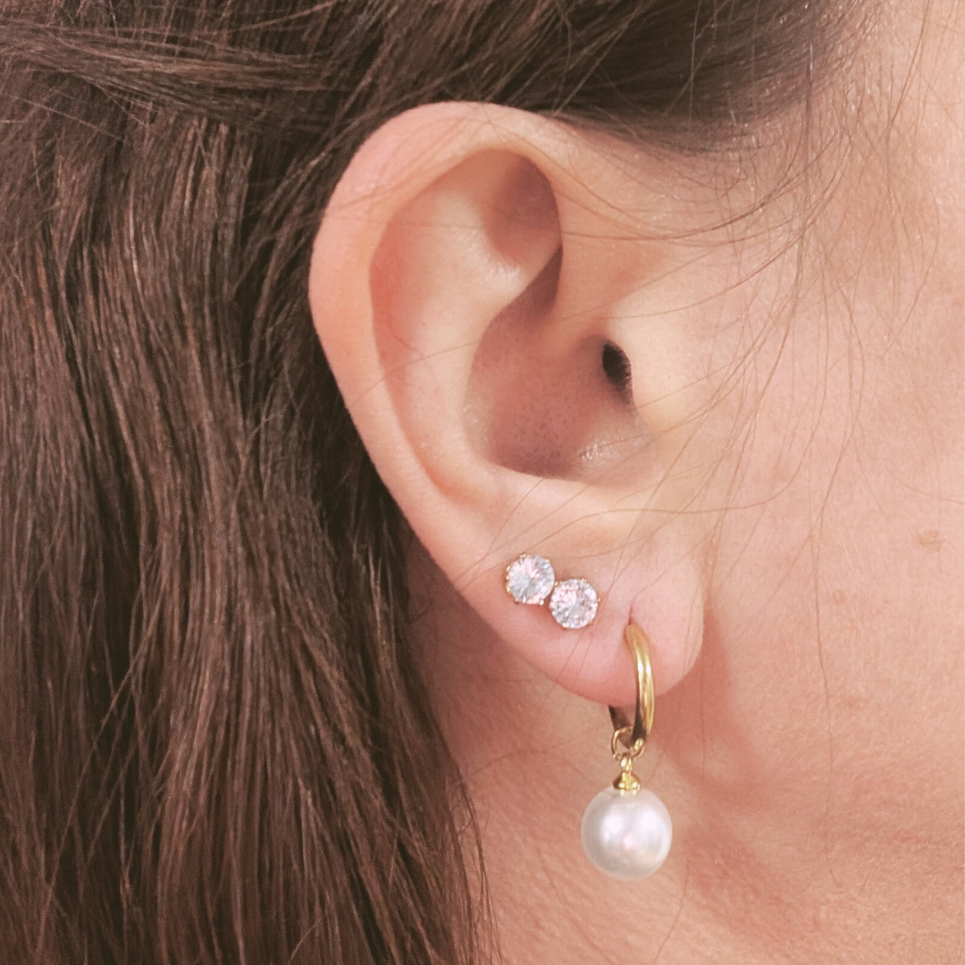 Close-up of an ear wearing gold hoop earrings with pearl drops and clear gemstones.