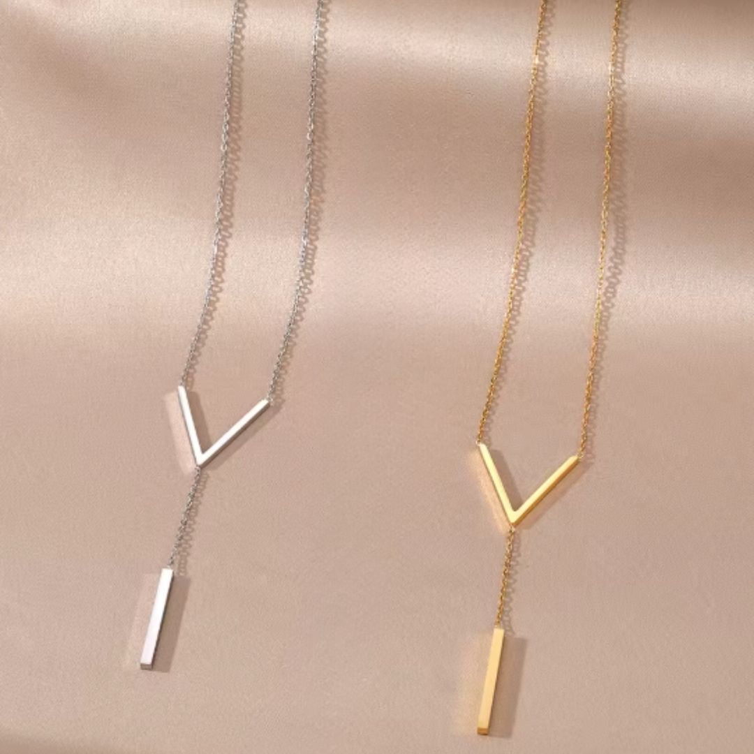 Two necklaces a gold and silver with geometric pendants on a beige fabric background