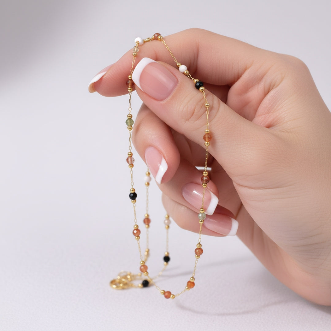 Hand holding a delicate beaded necklace against a light background