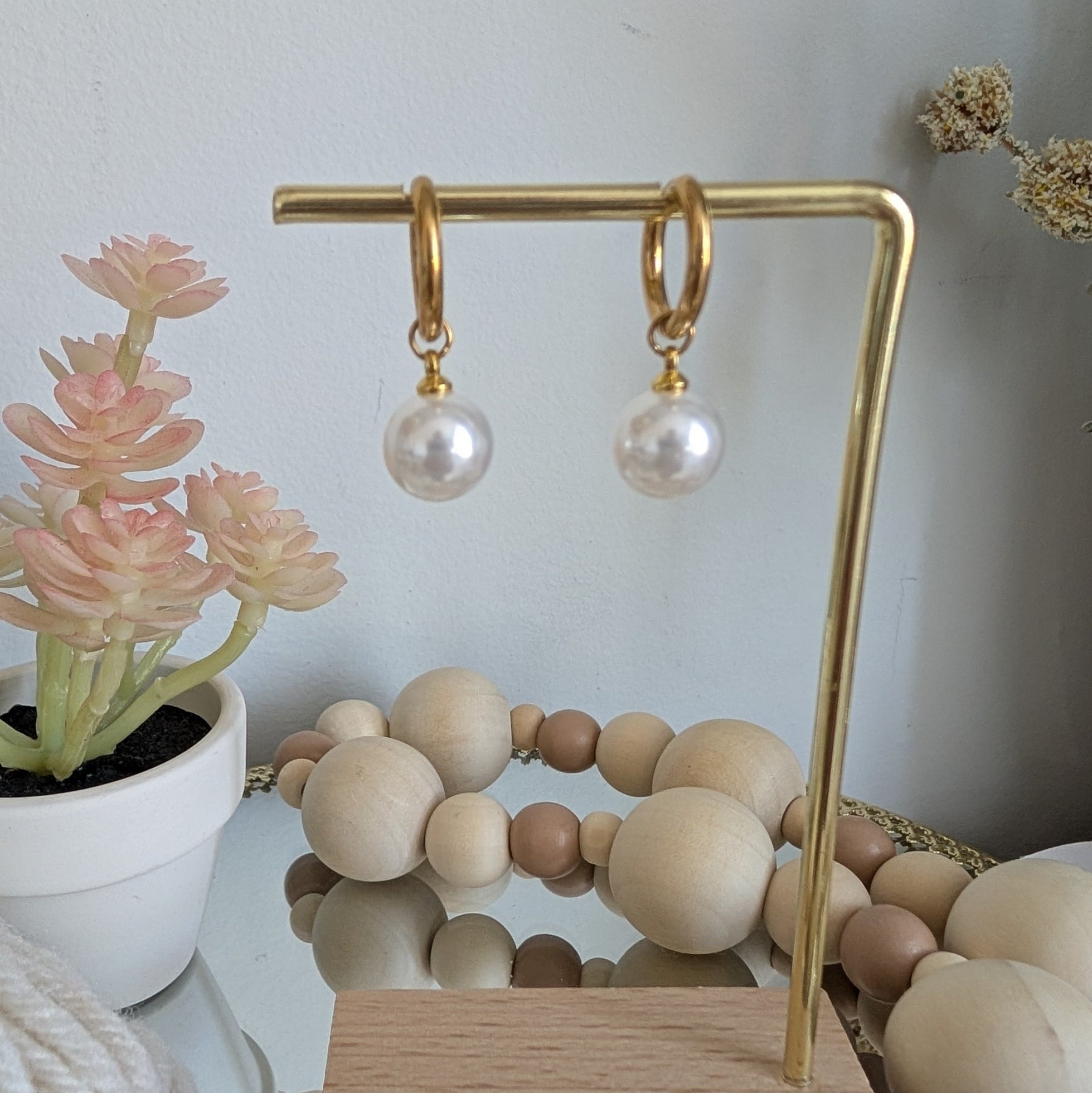 Pearl earrings on a gold earring stand with a wooden base, against a neutral background.
