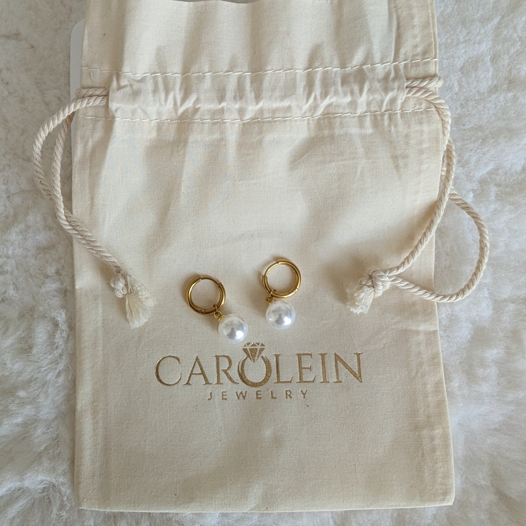 Gold earrings with pearls on a Carolein Jewelry pouch.