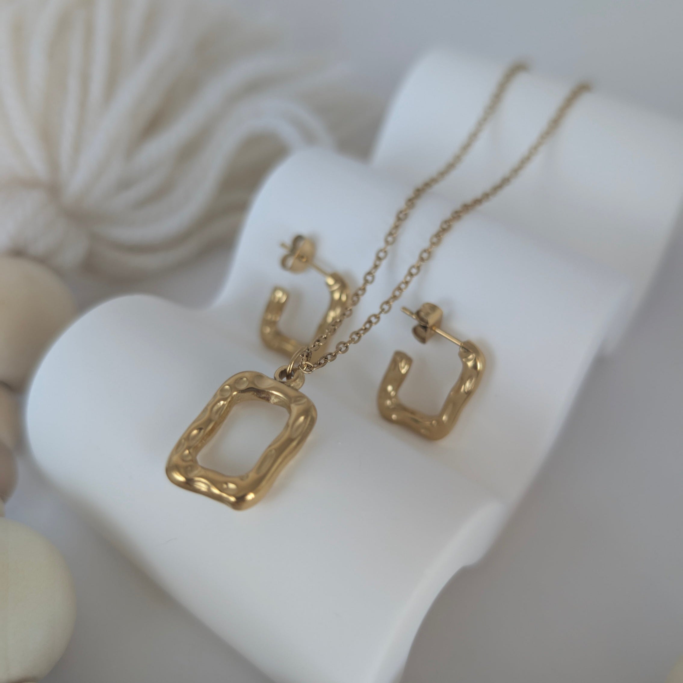 Gold necklace and earrings on a white stand with a neutral background