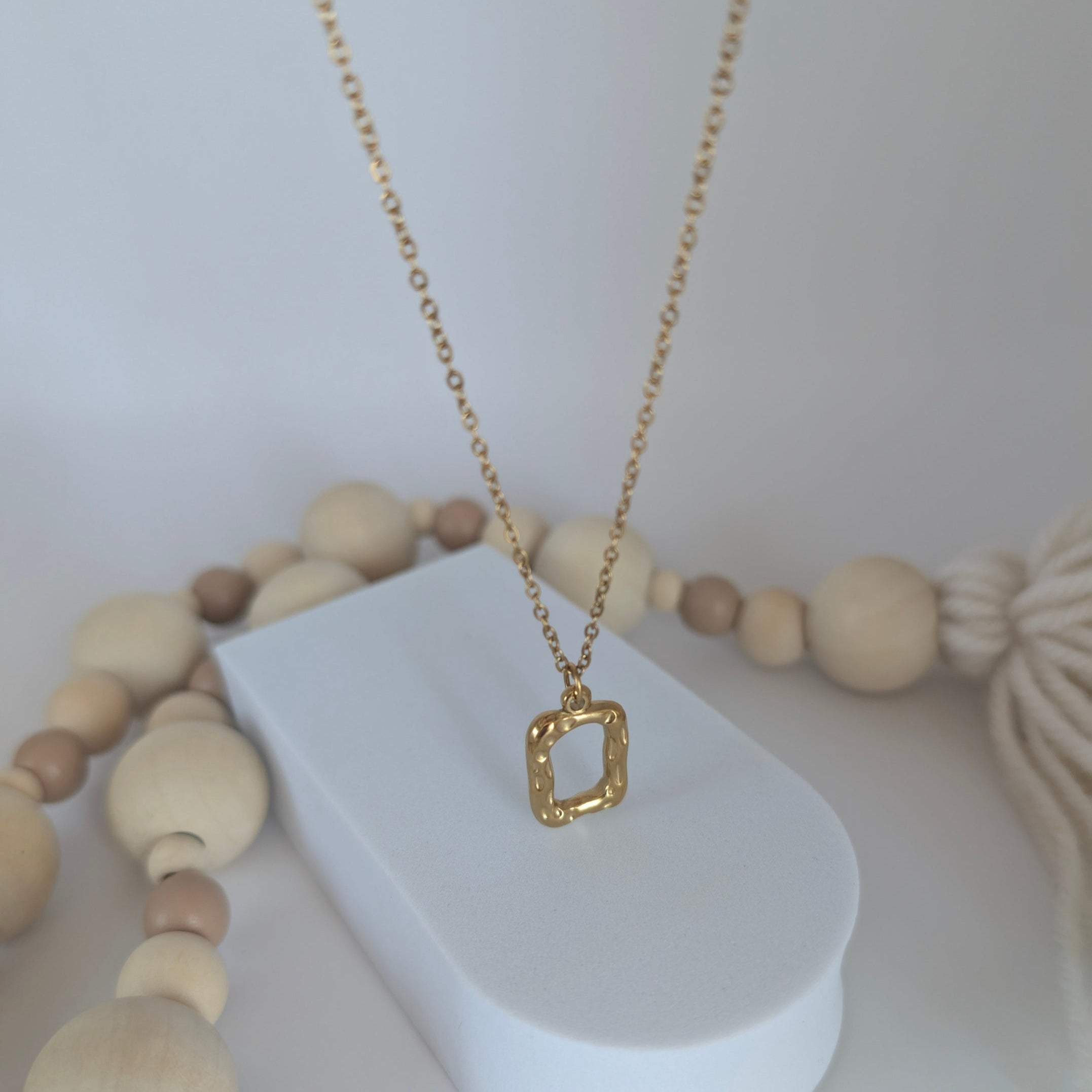 Gold necklace on a white stand with wooden beads in the background