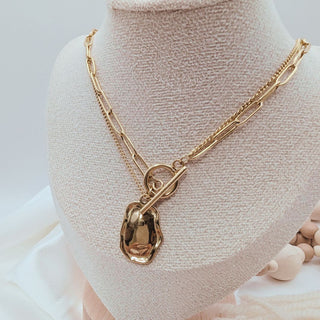 Gold necklace with a heart-shaped pendant on a mannequin bust.