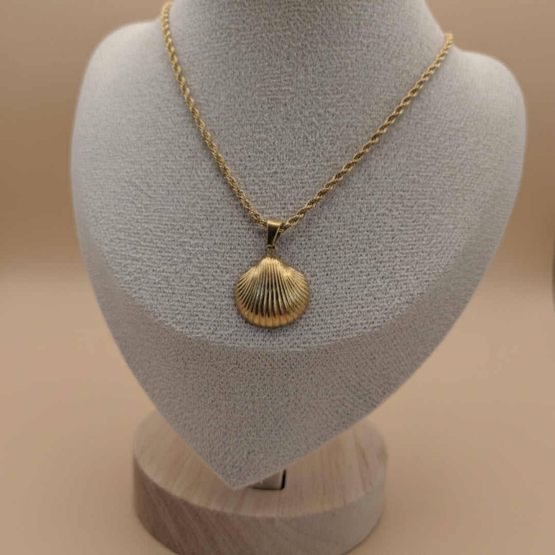 Gold necklace with a shell pendant on a mannequin bust against a beige background