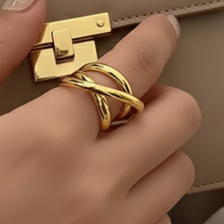 Gold ring on a finger with a beige handbag in the background