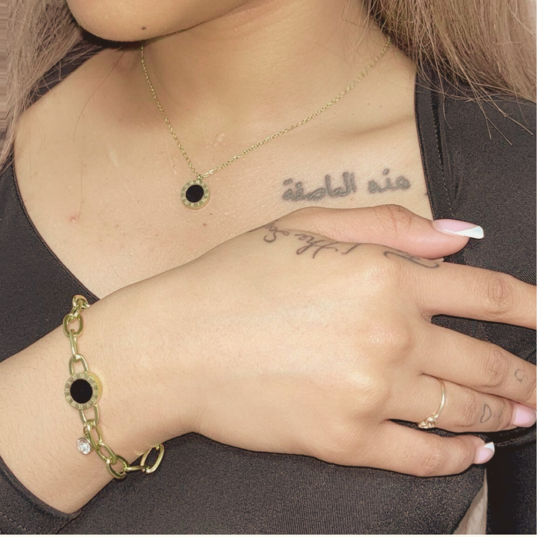 Close-up of a person wearing a gold bracelet with black stones, necklace, and ring.