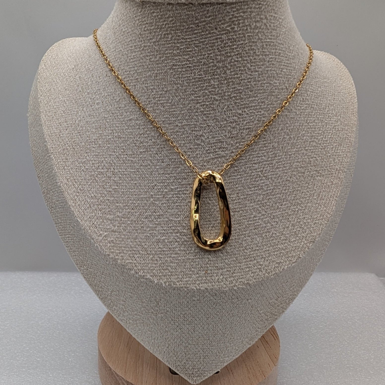 Gold necklace with a large pendant on a mannequin bust against a gray background