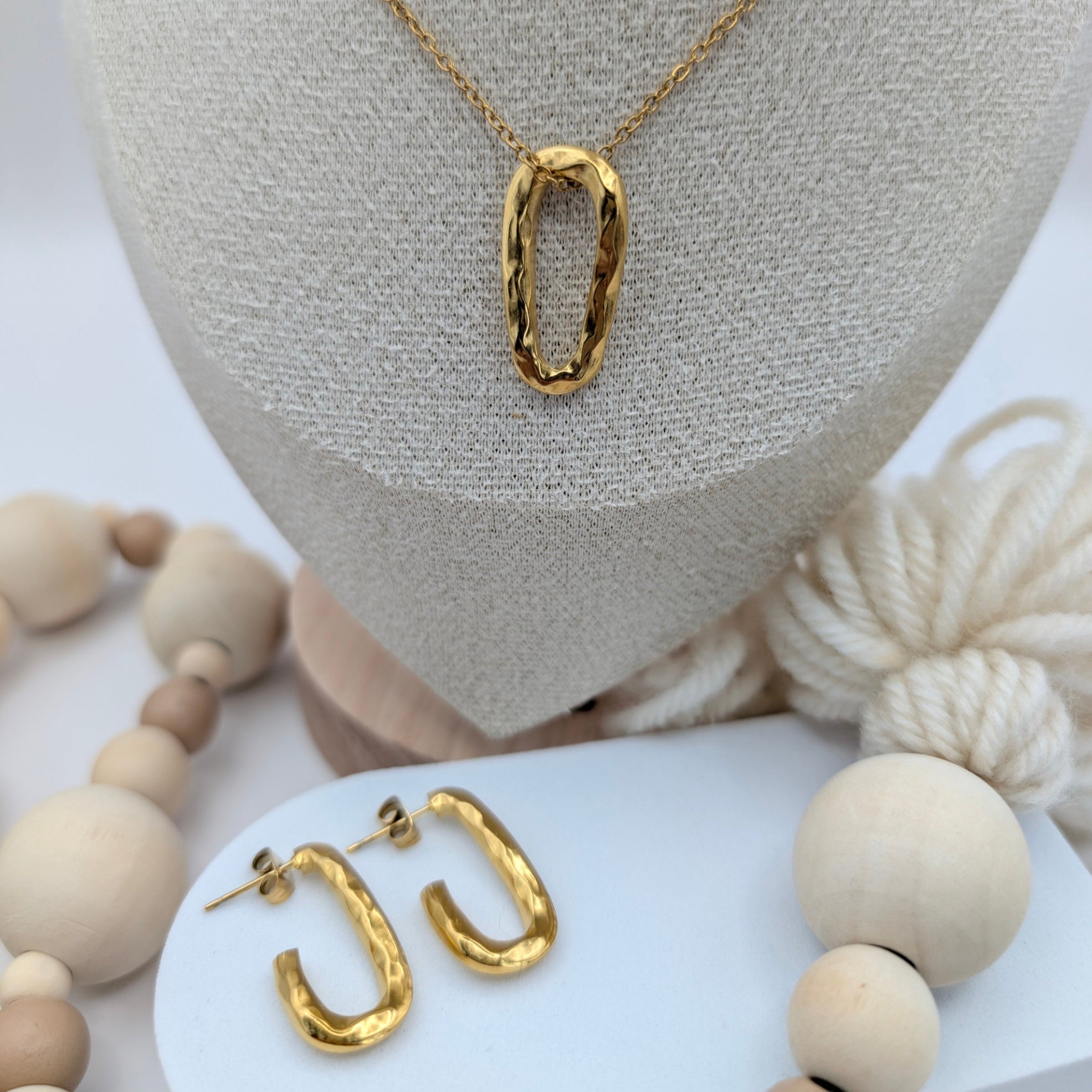 Gold necklace and hoop earrings on a white stand with wooden beads.