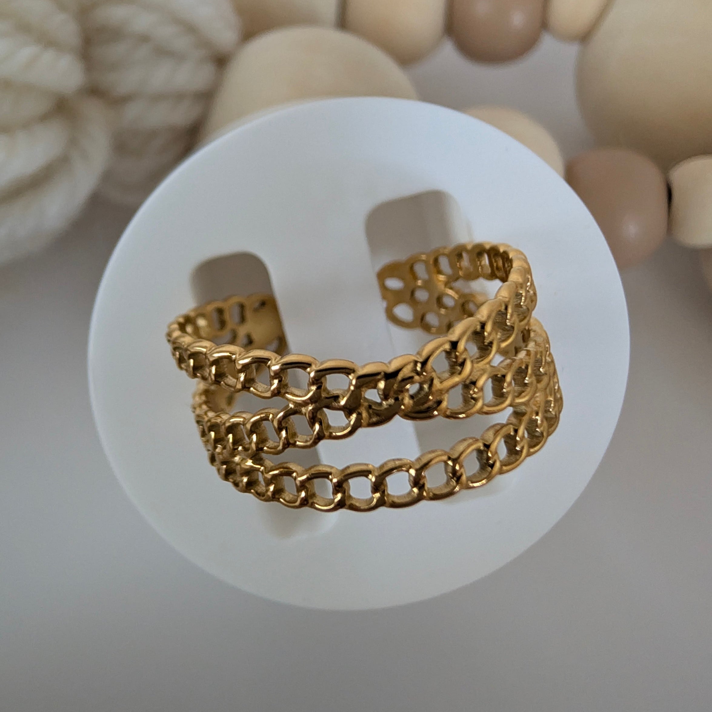 Gold chain ring on a white background with wooden beads in the background