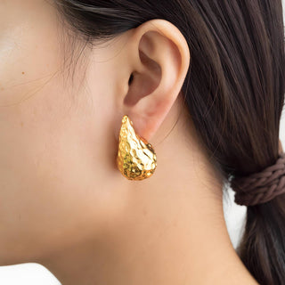 Gold earring worn by a person with a blurred background
