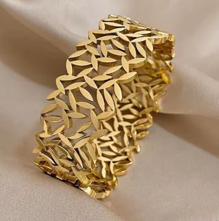 Gold bracelet with leaf-like pattern on a beige background