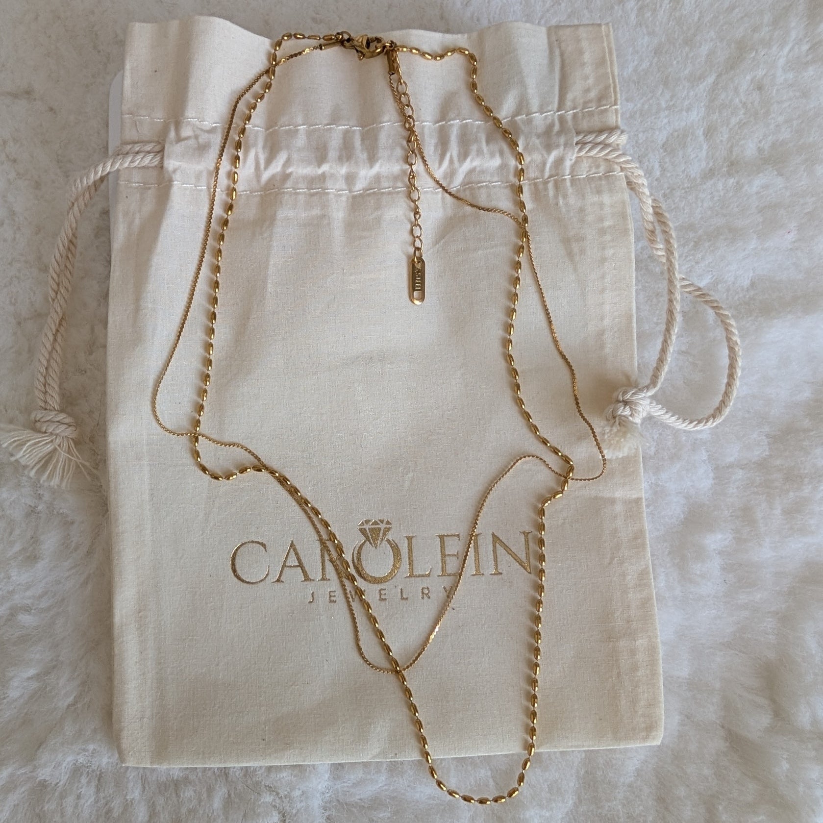 Gold necklace on a Caroline Jewelry pouch against a textured beige background