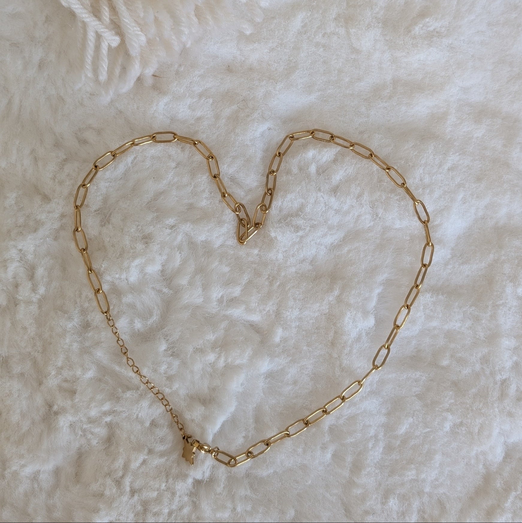 Gold chain necklace forming a heart shape on a soft white background