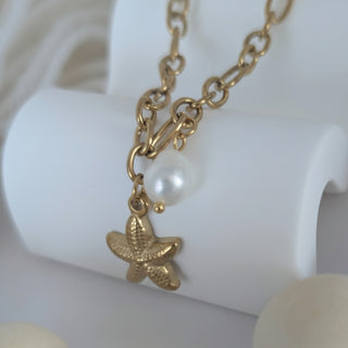 Gold chain necklace with a starfish charm and pearl on a white decor background