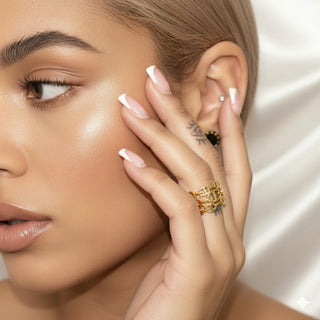 Close-up of a woman's face with a gold ring on her finger, against a neutral background