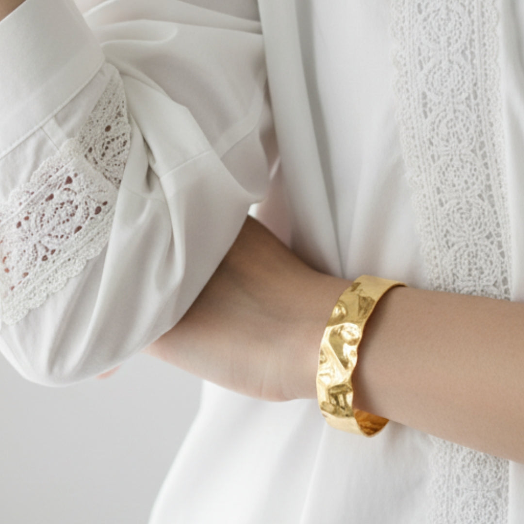 Gold BANGLE on a wrist with a white garment in the background