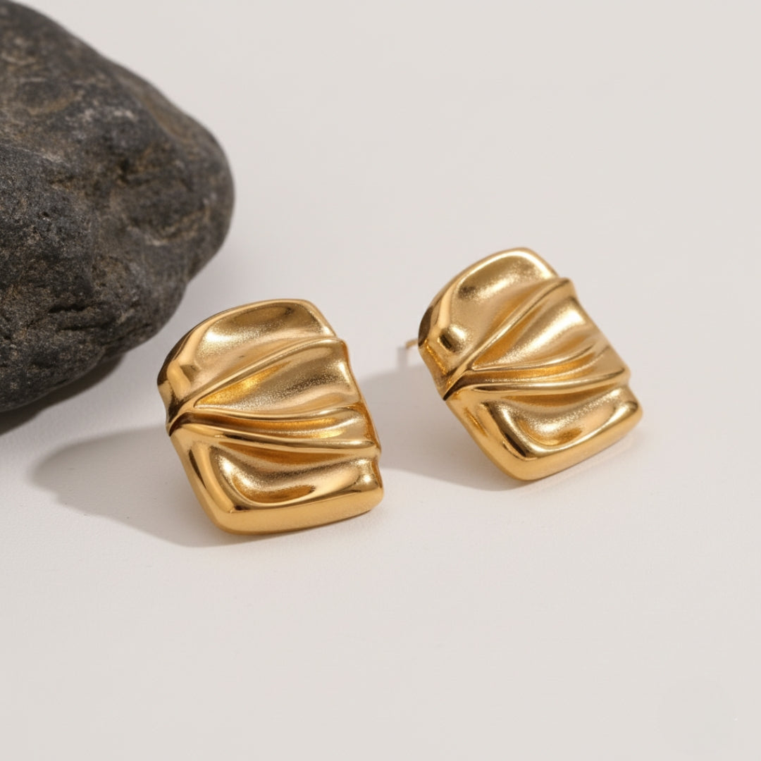 Gold earrings on a light background with a stone for scale