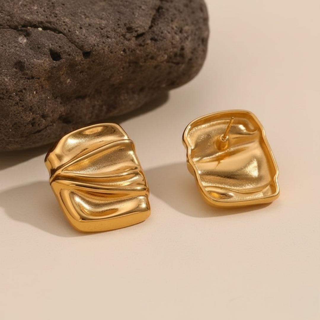 Gold earrings on a beige surface with a dark stone background