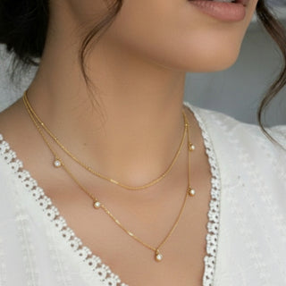 Close-up of a person wearing a gold necklace with pearl-like beads.