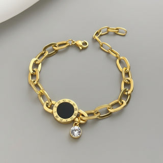 Gold chain bracelet with a black round charm and a clear crystal pendant on a gray background