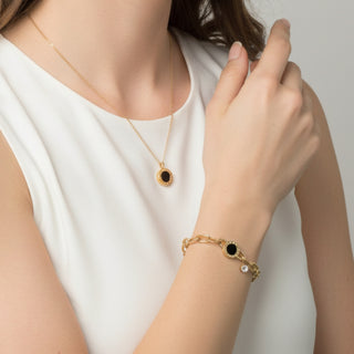 Woman wearing a gold bracelet and necklace with a black stone on a plain background