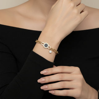 Gold bracelet with a black stone and clear gemstone on a person's wrist against a neutral background
