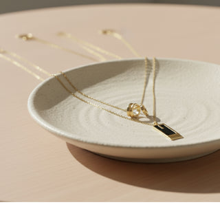 Gold necklace with a pendant on a white dish against a beige background