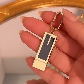 Gold and black rectangular pendant on a chain held by a hand.
