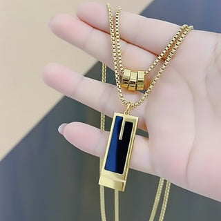 Gold necklace with a black pendant held by a hand against a neutral background