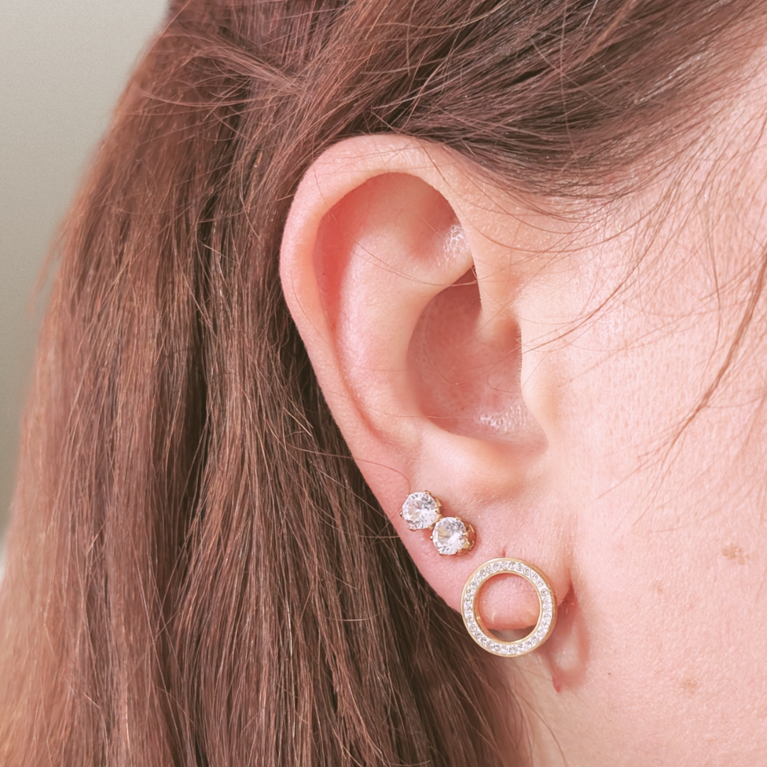 Close-up of an ear wearing gold hoop earrings with clear stones.