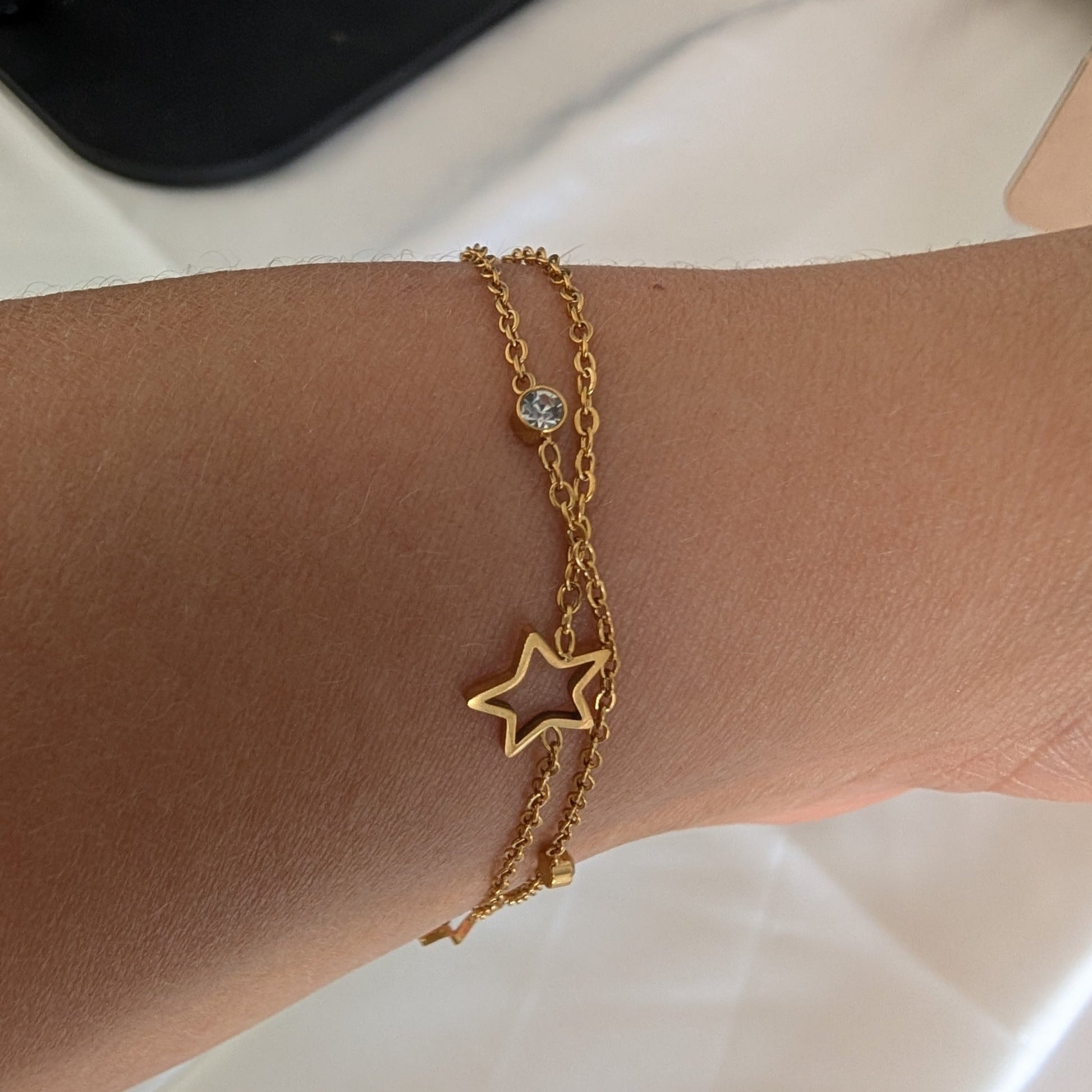 Gold star bracelet on a wrist with a neutral background
