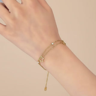 Gold bracelet with star charm on a wrist against a beige background