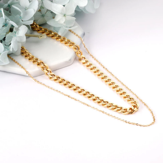 Gold chain necklace on a white surface with light greenery